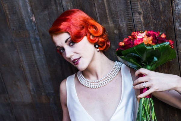 Model with vintage wedding dress, red hair with red bouquet, vintage pearl necklace and black and pearl earrings