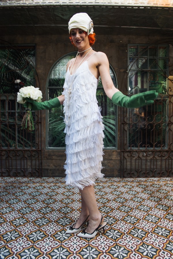 Model with red hair wearing white wedding flapper dress, vintage turban, long green gloves and white bouquet,